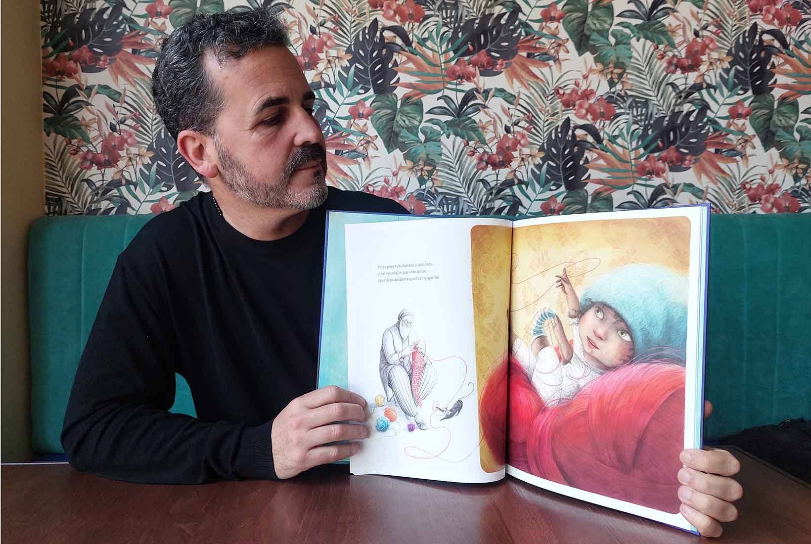 Ariel Andrés Almada muestra una página del interior de su libro 'Amor' donde aparece un bebé y un abuelo tejiendo ropa para él.