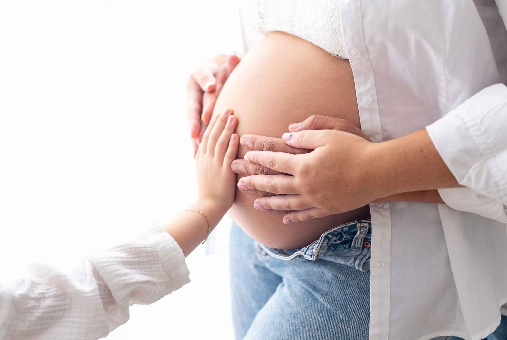 Fotografía de una mujer embarazada con las manos de su pareja e hija sobre la barriga. De Jennifer Suárez Fotografía.